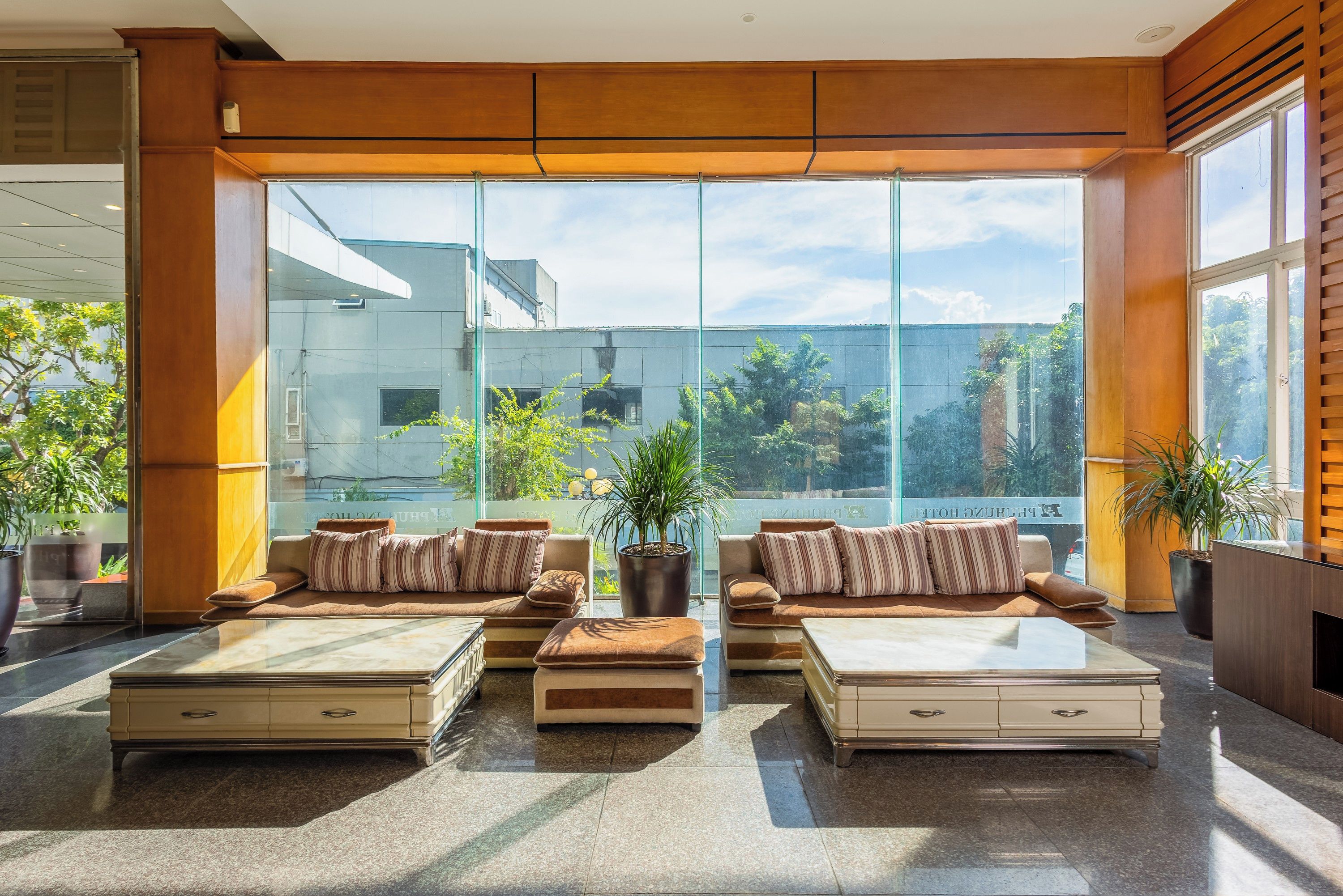 A spacious lobby with a modern design, featuring a large seating area with sofas and armchairs, a coffee table, and a large window offering a view of the cityscape.