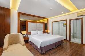 Habitación de hotel moderna con una cama grande, zona de estar, televisor y cabina de ducha de vidrio.