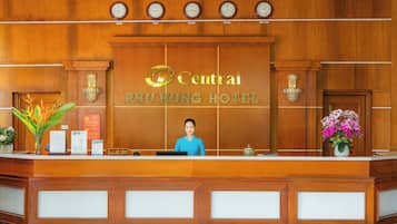 A hotel reception desk with clocks displaying times from various cities, a receptionist, and floral arrangements.