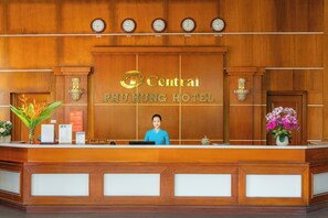 A hotel reception desk with clocks displaying times from various cities, a receptionist, and floral arrangements.