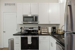 A modern kitchen with white cabinets, a stainless steel microwave, a stove, and a refrigerator. - Sweetheart City Downtown Retreat | Dog Friendly (Loveland)