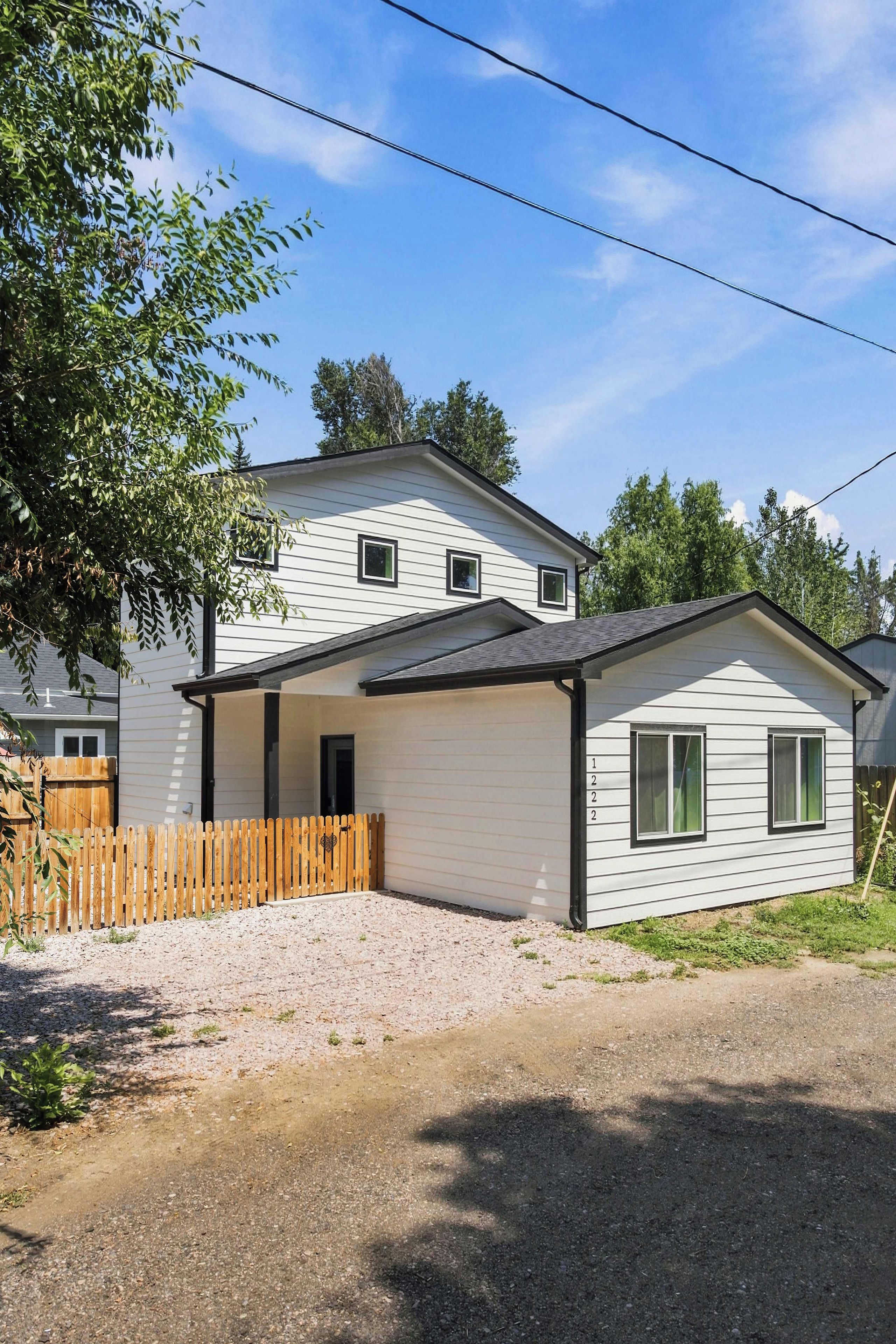 A single-story house with a covered porch, a wooden fence, and a gravel driveway.