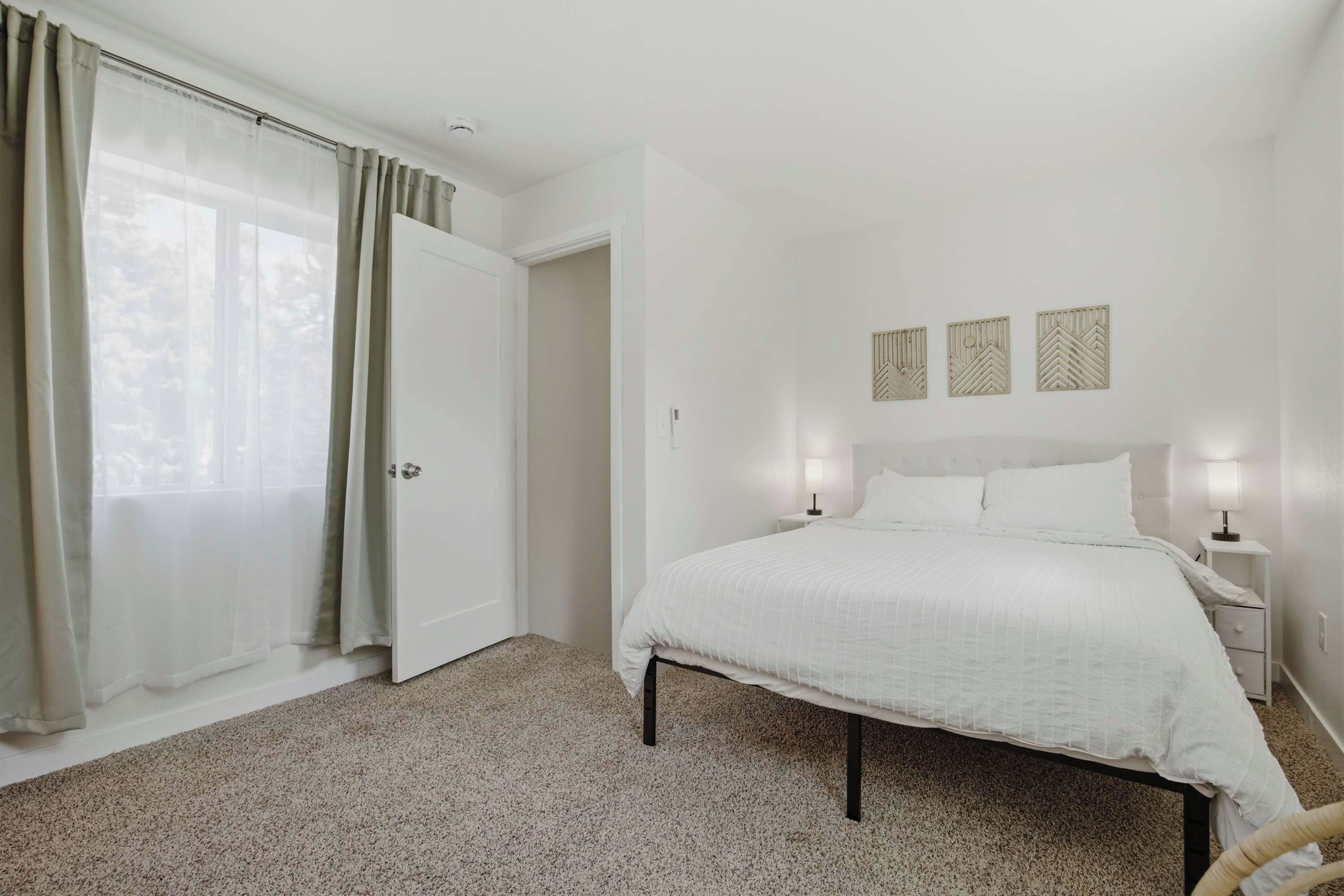 Un dormitorio con cama, mesita de noche, lámpara, puerta y ventana con cortinas.