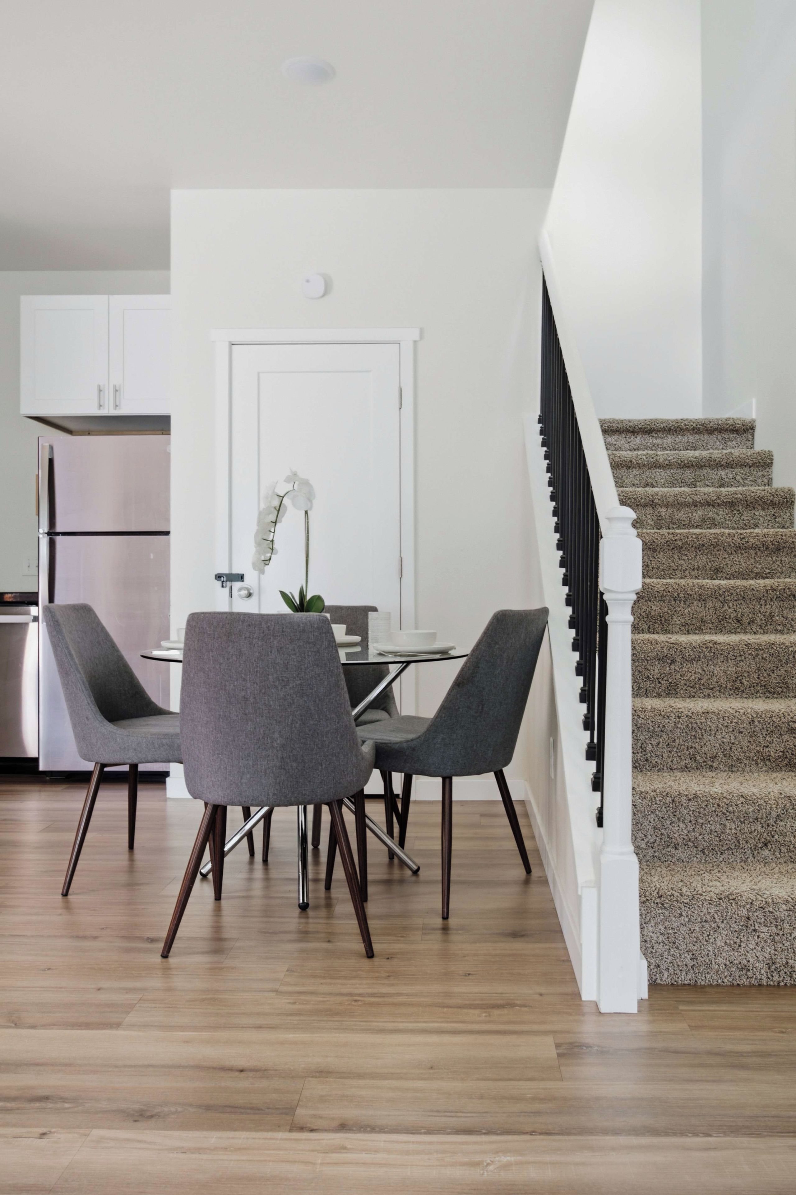 A modern kitchen with white cabinets, a double-door refrigerator, and a dining area with a glass table and two grey chairs.
