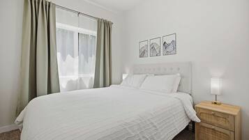 Une chambre à coucher avec un lit, une table de chevet, une lampe et une fenêtre avec des rideaux.