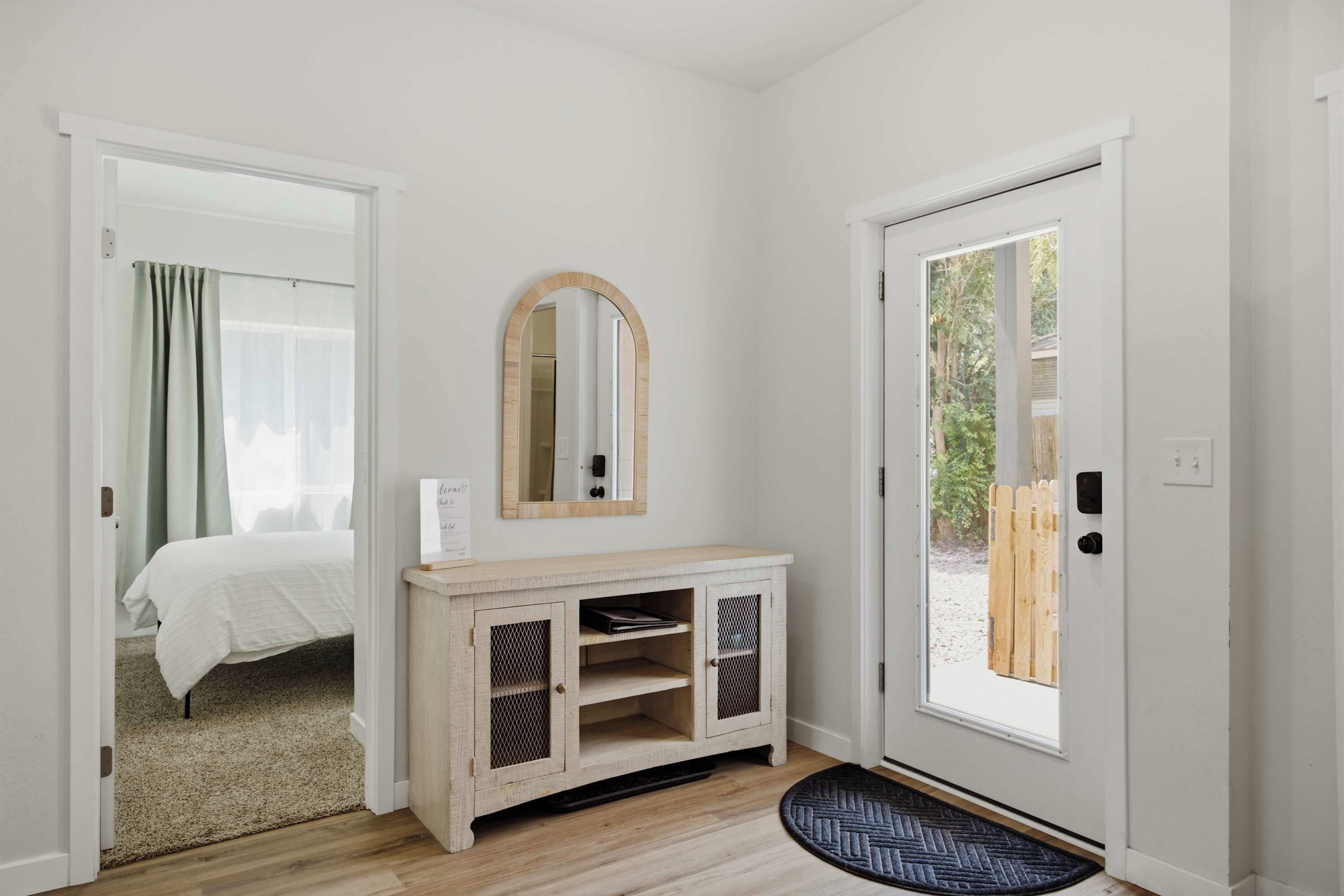 A room with a bed, a mirror, a wooden console, and a door leading outside.