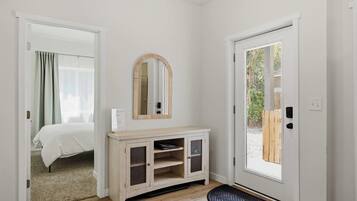 A room with a bed, a mirror, a wooden console, and a door leading outside.