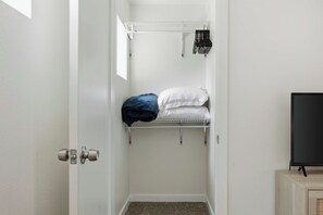 A narrow walk-in closet with a metal shelf, a hanging rack, and a door with a round handle. - Sweetheart City Downtown Retreat | Dog Friendly (Loveland)