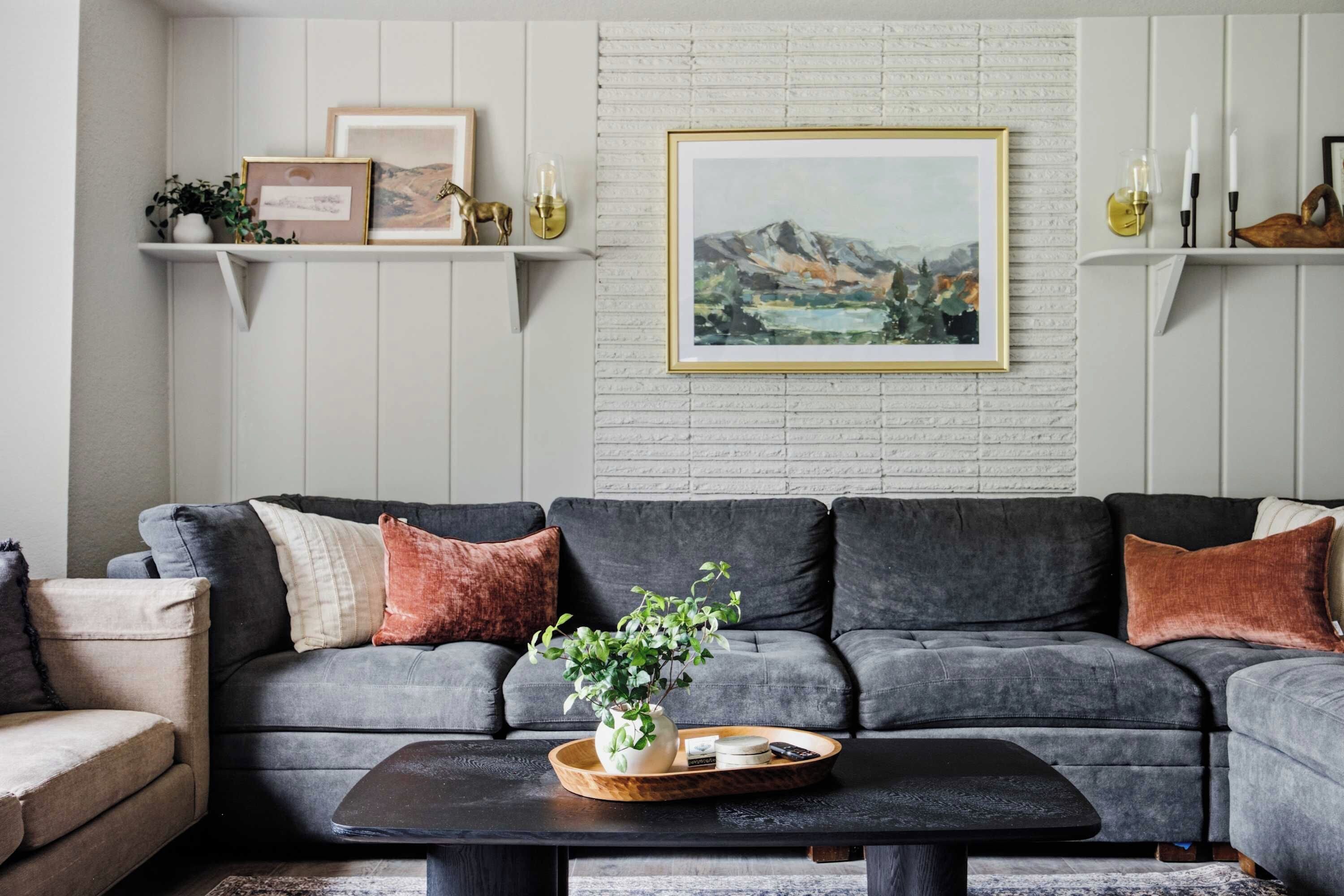 Una sala de estar moderna con un sofá seccional gris, una mesa de centro con una planta y obras de arte enmarcadas en la pared.