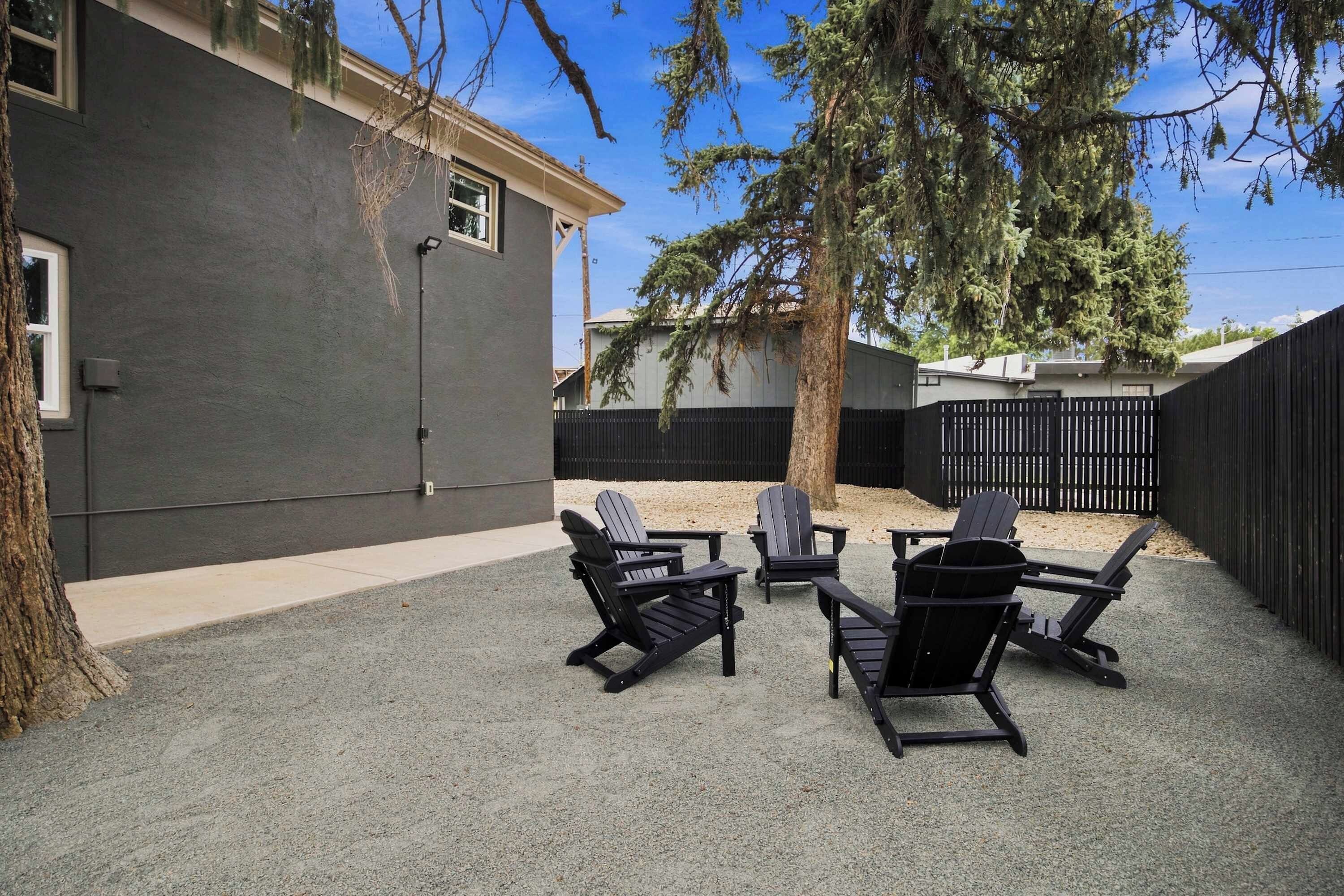 Un patio trasero con suelo de grava, sillas Adirondack negras y cerca de madera.