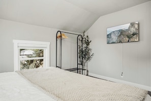 A bedroom with a bed, a window, a plant, and a painting on the wall. - The Evergreen Home | King Beds + Fire Pit (Loveland)