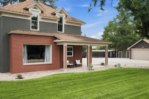 A two-story house with a covered patio, a garage, and a well-maintained lawn. - The Evergreen Home | King Beds + Fire Pit (Loveland)