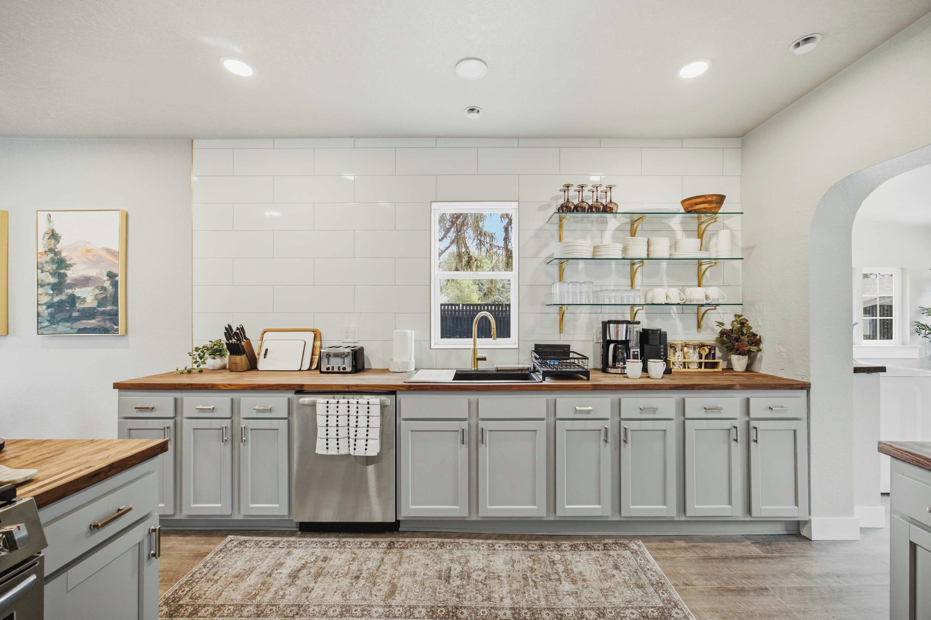 A modern kitchen with grey cabinets, a wooden countertop, and a stainless steel dishwasher.
