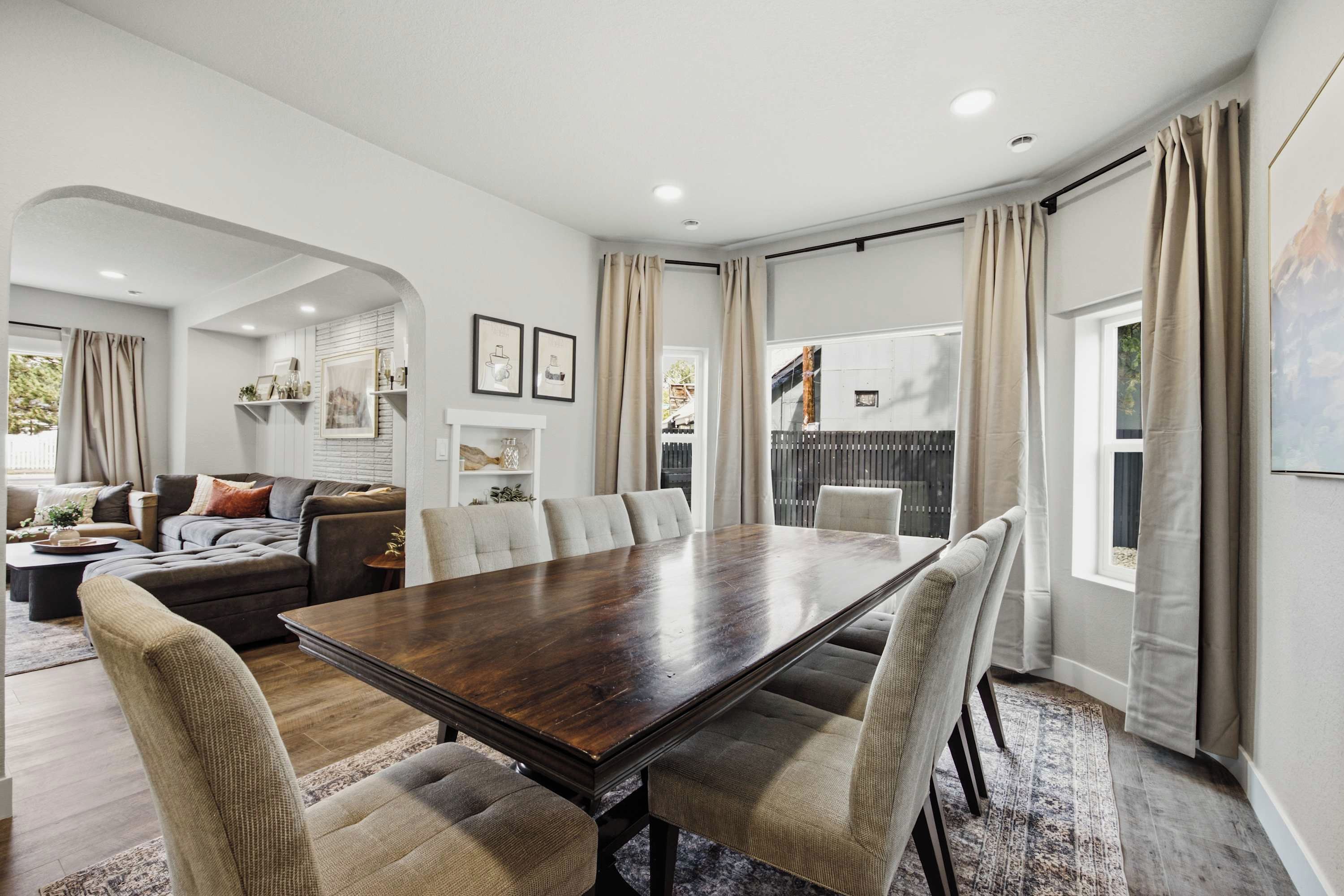 Un comedor amplio con una gran mesa de madera y sillas tapizadas, rodeado por una sala de estar con sofá y chimenea.