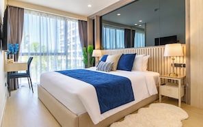 A modern hotel room with a large bed, a desk, a chair, and a TV. - OZON OASIS Apartment by TVC (Choeng Thale)
