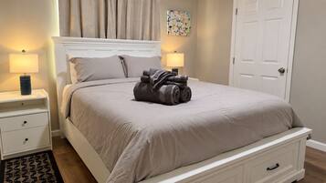 A neatly made bed with a headboard, two bedside tables with lamps, a door, and a wall with a floral painting.