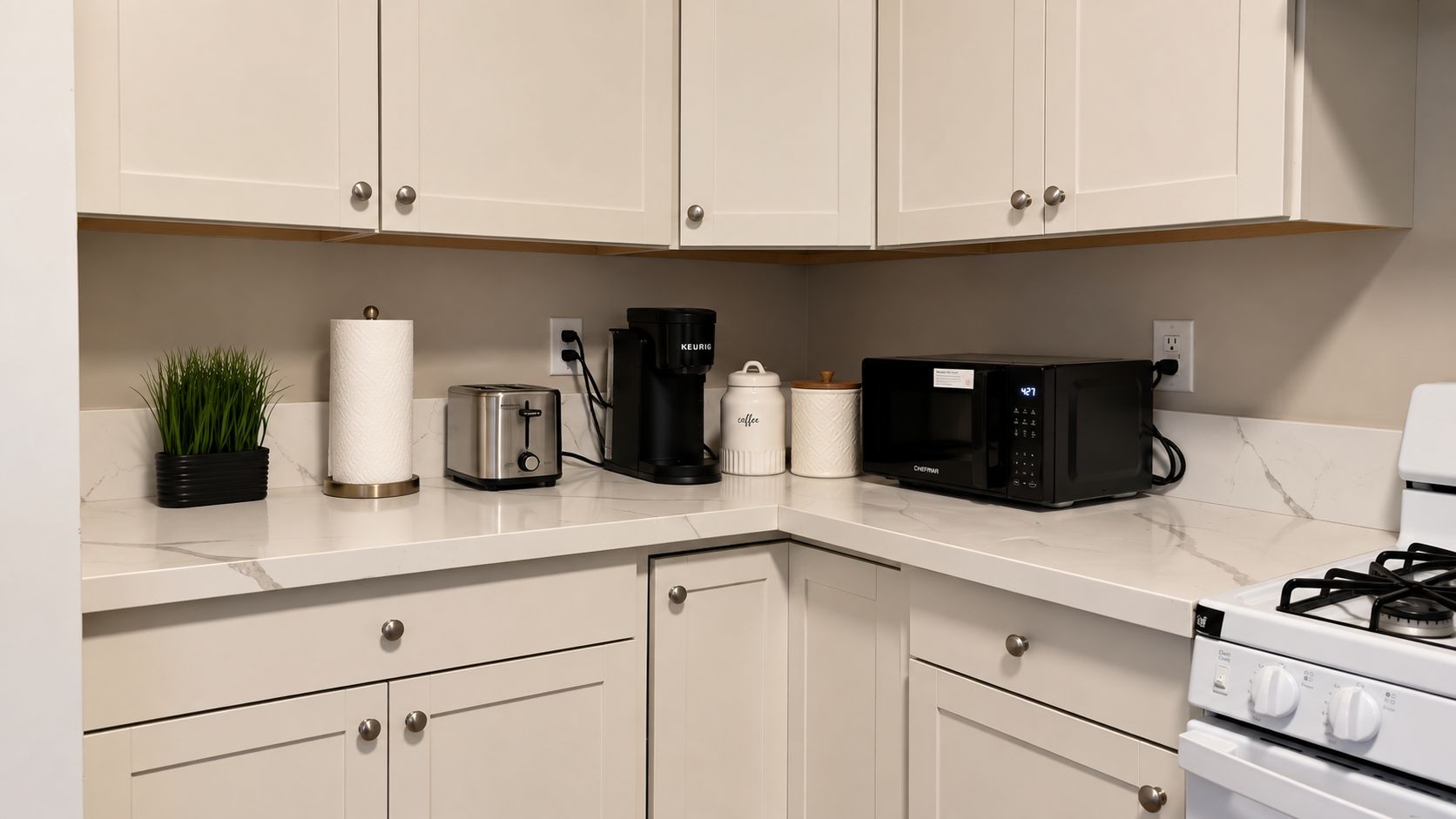 Una cocina con armarios blancos, un tostador, una cafetera, un microondas y una estufa.
