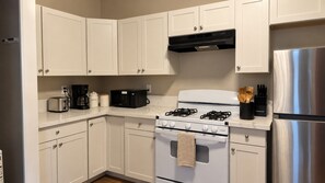 Eine Küche mit weißen Schränken, einem Edelstahl-Kühlschrank, einem Gasherd und einer Kaffeemaschine.