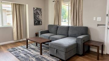 A living room with a grey sectional sofa, two wooden side tables, and a patterned rug.