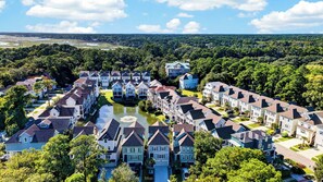Un quartier résidentiel où les maisons sont disposées en rangées, avec une fontaine centrale et une forêt dense en arrière-plan.
