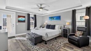 Une chambre à coucher moderne, avec un lit, des tables de chevet, une chaise, un ventilateur de plafond et des œuvres d’art accrochées aux murs.