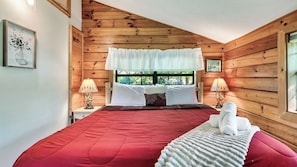 A wooden cabin-style bedroom with a red bedspread, two bedside lamps, and a window with a view of greenery. - Hibernation Station by Avantstay Hot Tub + Theater Room + Mtn Views Mins to Dollywood + Smokies (Sevierville)