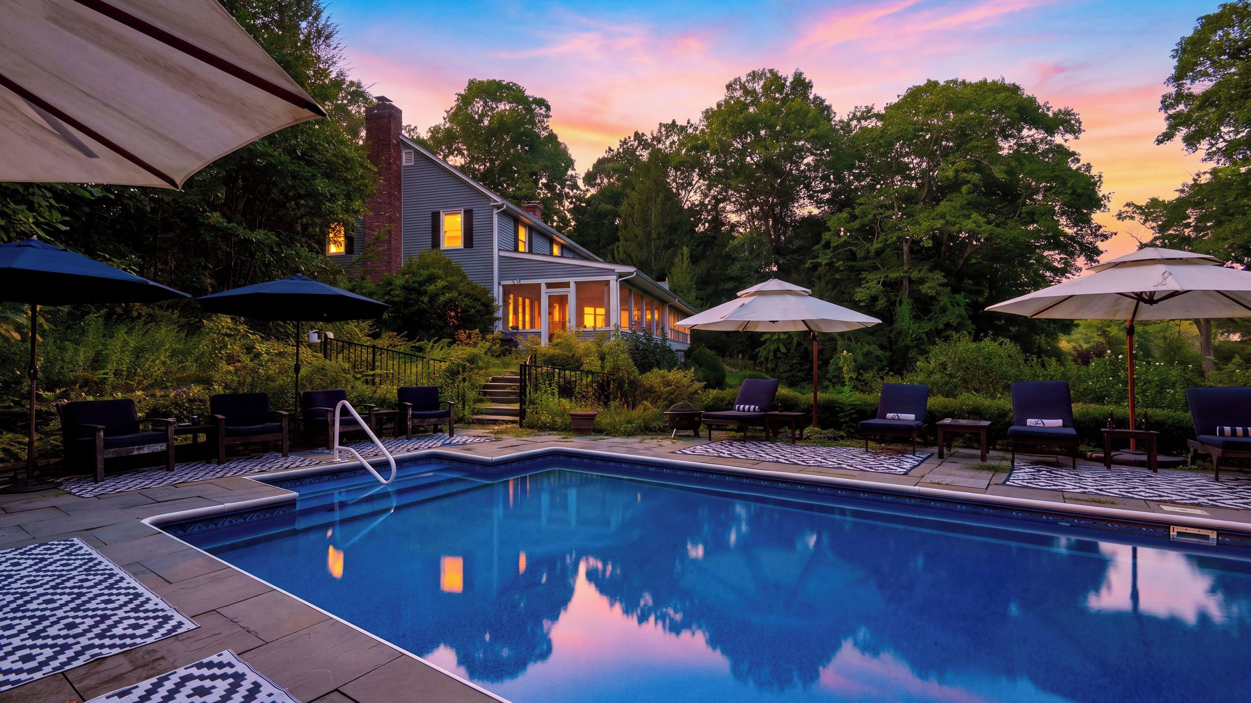 A swimming pool with lounge chairs and umbrellas, surrounded by trees and a house.
