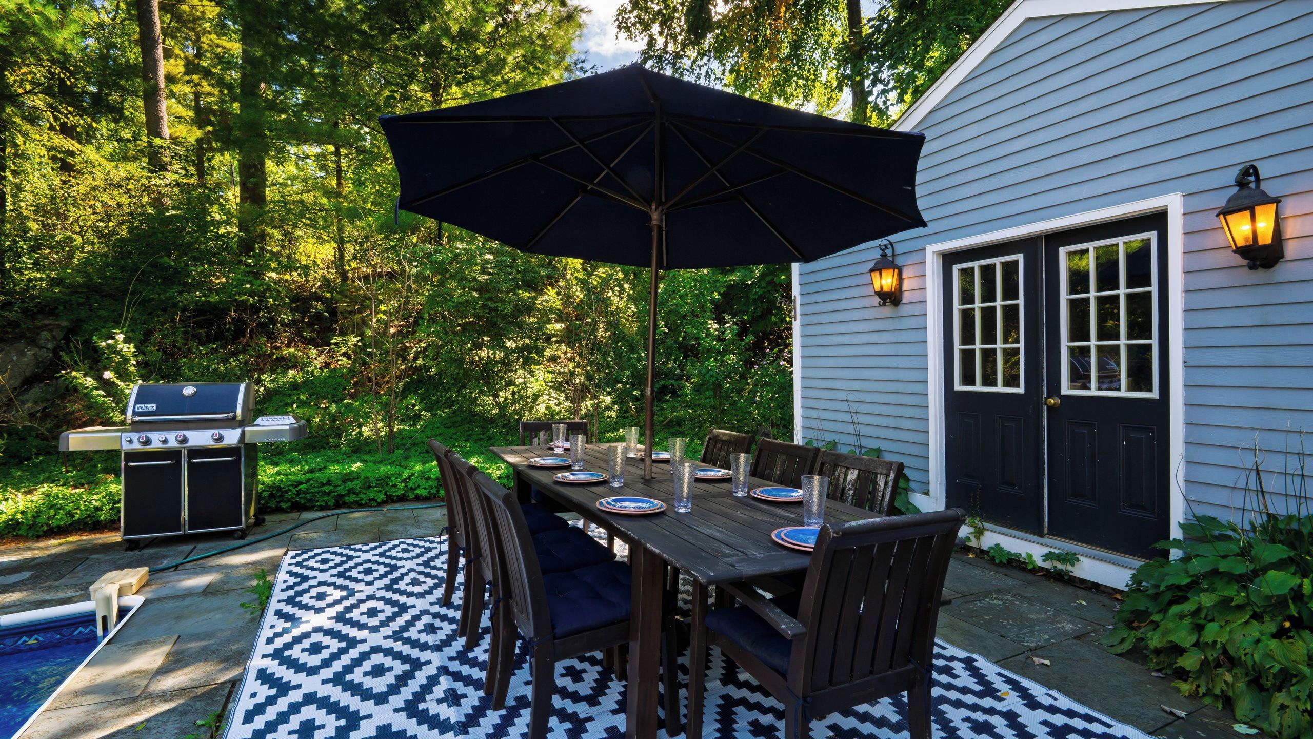 An outdoor dining area with a table set for four, surrounded by chairs, under a large umbrella.