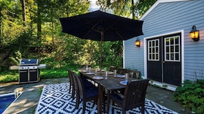 An outdoor dining area with a table set for four, surrounded by chairs, under a large umbrella.