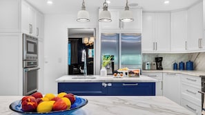Cozinha moderna com armários brancos, uma parede de destaque azul, uma ilha grande com uma fruteira e uma cafeteira.