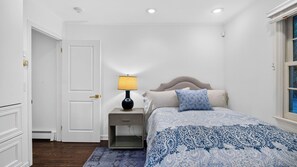 A bedroom with a bed, nightstand, lamp, and a door.