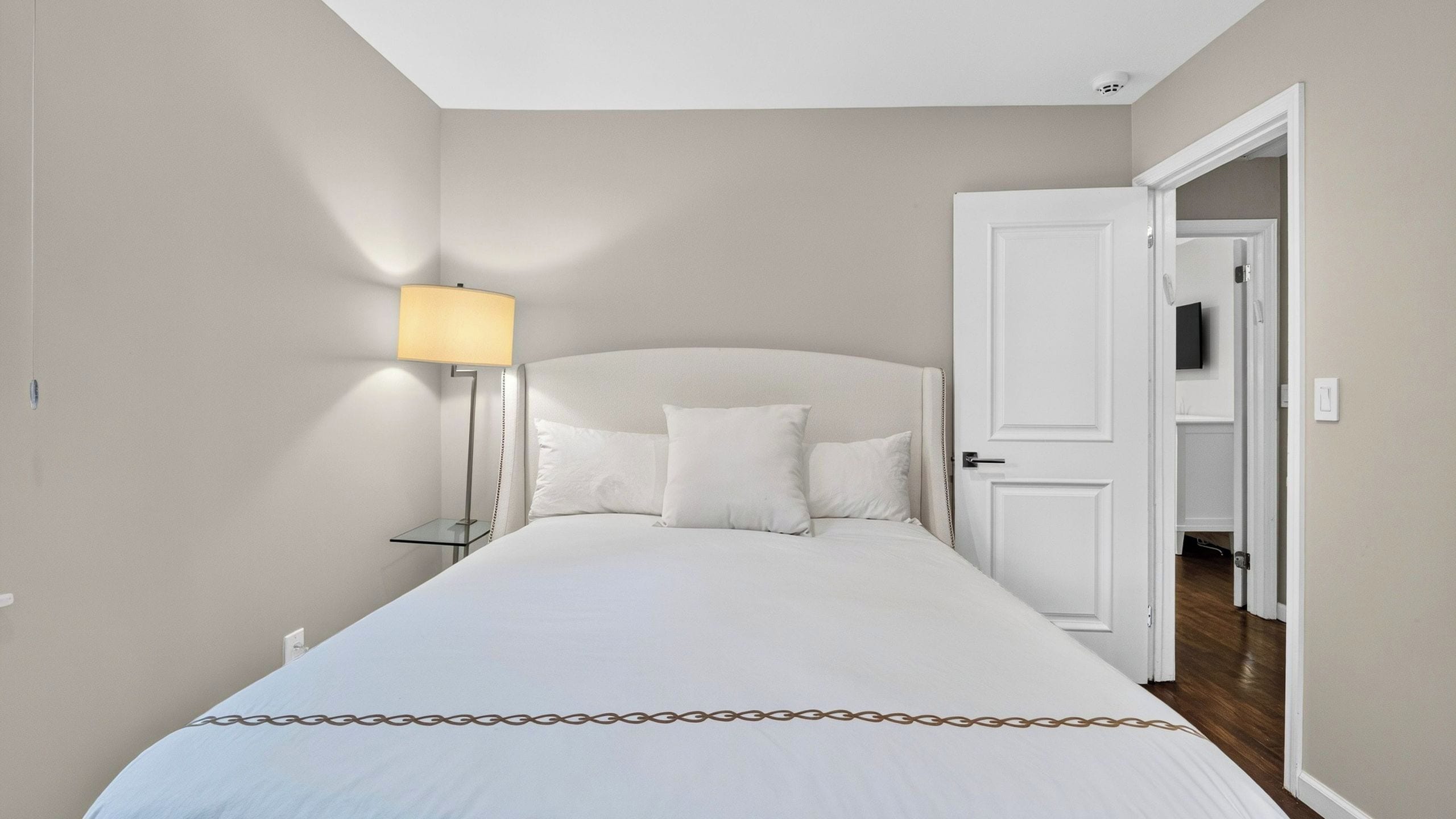 A bedroom with a bed, a bedside lamp, and a door leading to another room.