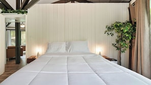 Quarto com uma cama grande, duas mesas de cabeceira, um criado-mudo, uma planta em vaso e uma janela com cortinas.
