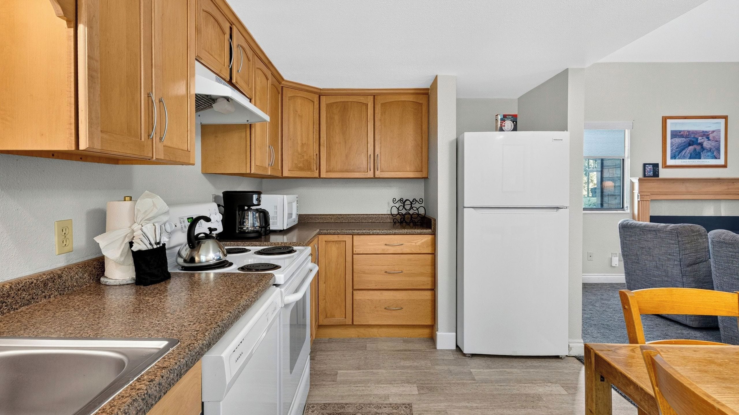 Una cocina compacta con armarios de madera, un refrigerador blanco, una estufa y una cafetera.