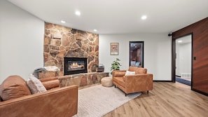 Ein modernes Wohnzimmer mit Kamin aus Stein, Ledersofas und Holzboden.