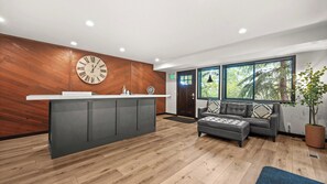 Eine moderne Küche mit einer Wand aus Holzverkleidung in Fischgrätmuster, einer großen Uhr und einer integrierten Kücheninsel mit Spüle.