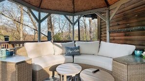 A covered outdoor seating area with a curved white sofa, a small round table, and wicker furniture. - Happy Trails by Avantstay Wraparound Deck + Hot Tub Near Dollywood + Pigeon Forge (Sevierville)