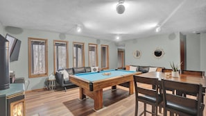 Ein Zimmer mit Pooltisch, einer Couch, einem Esstisch mit Stühlen und einem Fernseher.