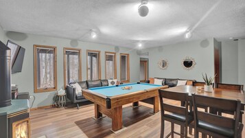 Una habitación con mesa de billar, sofá, mesa de comedor con sillas y televisor.