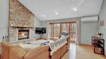 Una sala de estar con chimenea de piedra, televisor de pantalla plana, sofá de cuero y vistas a través de puertas de vidrio.
