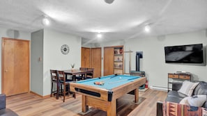 Ein Zimmer mit Billardtisch, Fernseher, einer Couch und einer Tür.