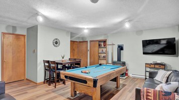 Una habitación con mesa de billar, televisor, sofá y una puerta.