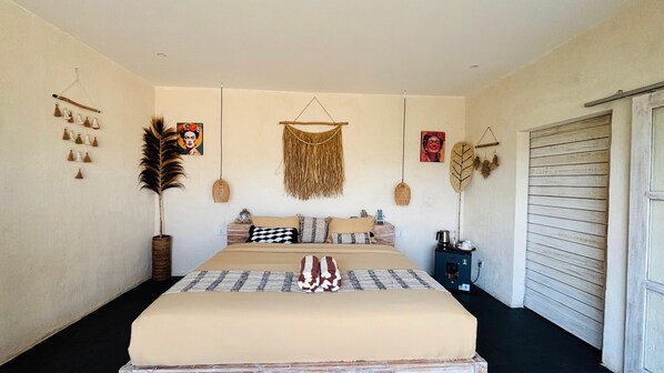 A bedroom with a large bed, a bedside table with a lamp, and a wall-mounted tapestry.