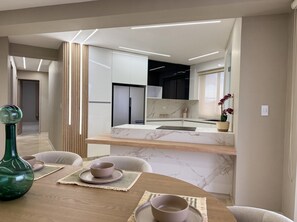 Una cocina moderna con encimera de mármol, comedor con mesa de madera y vista al salón contiguo.