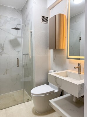 Un baño moderno con cabina de ducha de vidrio, inodoro blanco y tocador con espejo.