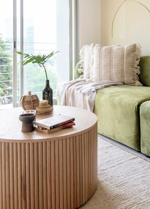 Une pièce avec une table ronde en bois, un canapé vert et une grande fenêtre donnant sur un paysage verdoyant.