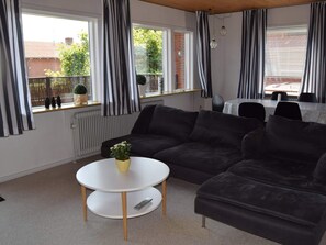 A modern living room with a sectional sofa, a round coffee table, and a dining area with a table and chairs. - 4 Star Holiday Home in Strandby (Strandby)