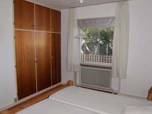 A bedroom with a wooden wardrobe, a window with curtains, a radiator, and a bed. - 4 Star Holiday Home in Strandby (Strandby)
