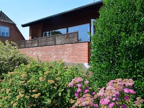 A modern two-story house with a brick facade, a balcony, and a well-maintained garden with various shrubs and flowers. - 4 Star Holiday Home in Strandby (Strandby)