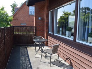 A balcony with a metal table and two chairs, a wooden fence, and a brick building in the background. - 4 Star Holiday Home in Strandby (Strandby)